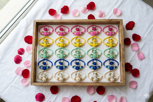 Colourful floral ring and bracelet combos in pink, yellow, green, blue and pearl white arranged neatly in a wooden tray on white cloth with rose petals scattered around for wedding return gift packaging