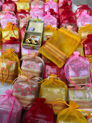Colorful organza potli bags packed in a traditional Pichwai box with roli chawal plate for wedding and pooja gifting